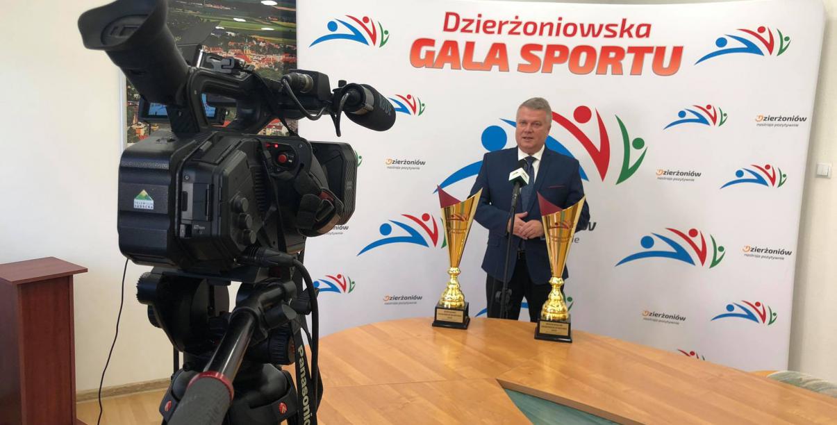 Burmistrz Dzierżoniowa na ściance promocyjnej ze sportowymi pucharami