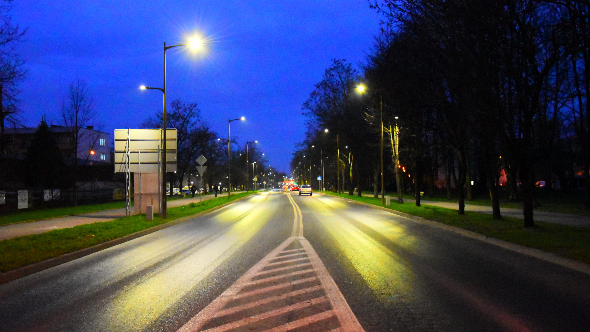 Dwupasmow droga nocą, po bokach świecące lampy, ciemnoniebieskie niebo