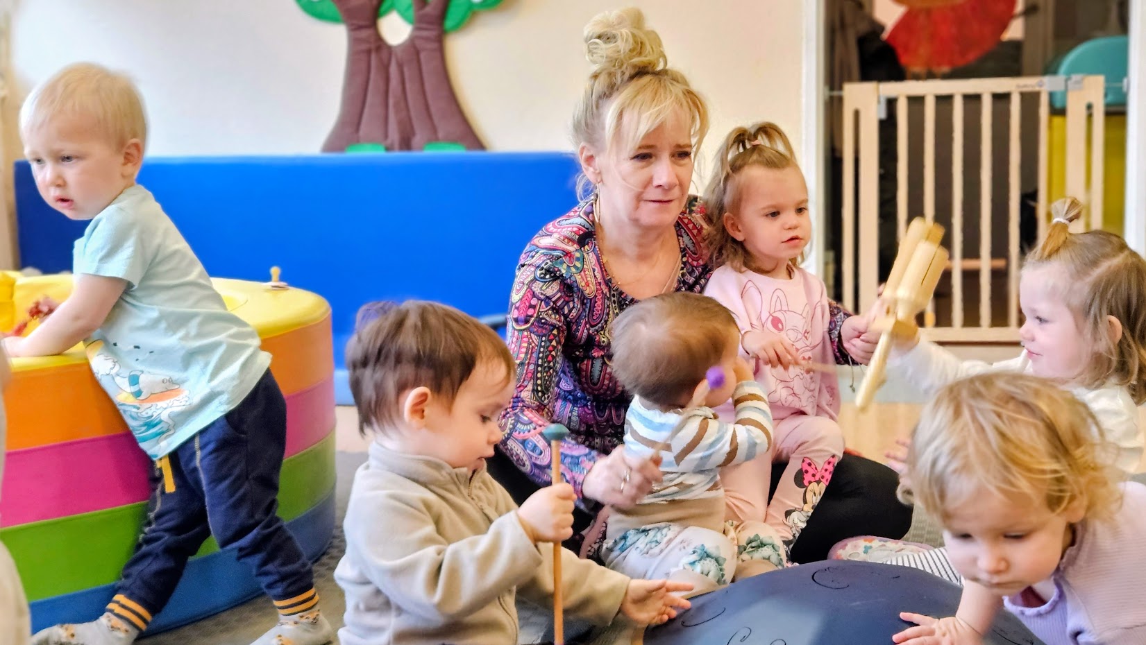 małe dzieci grają na instrumetach perskusyjnych z opiekunką