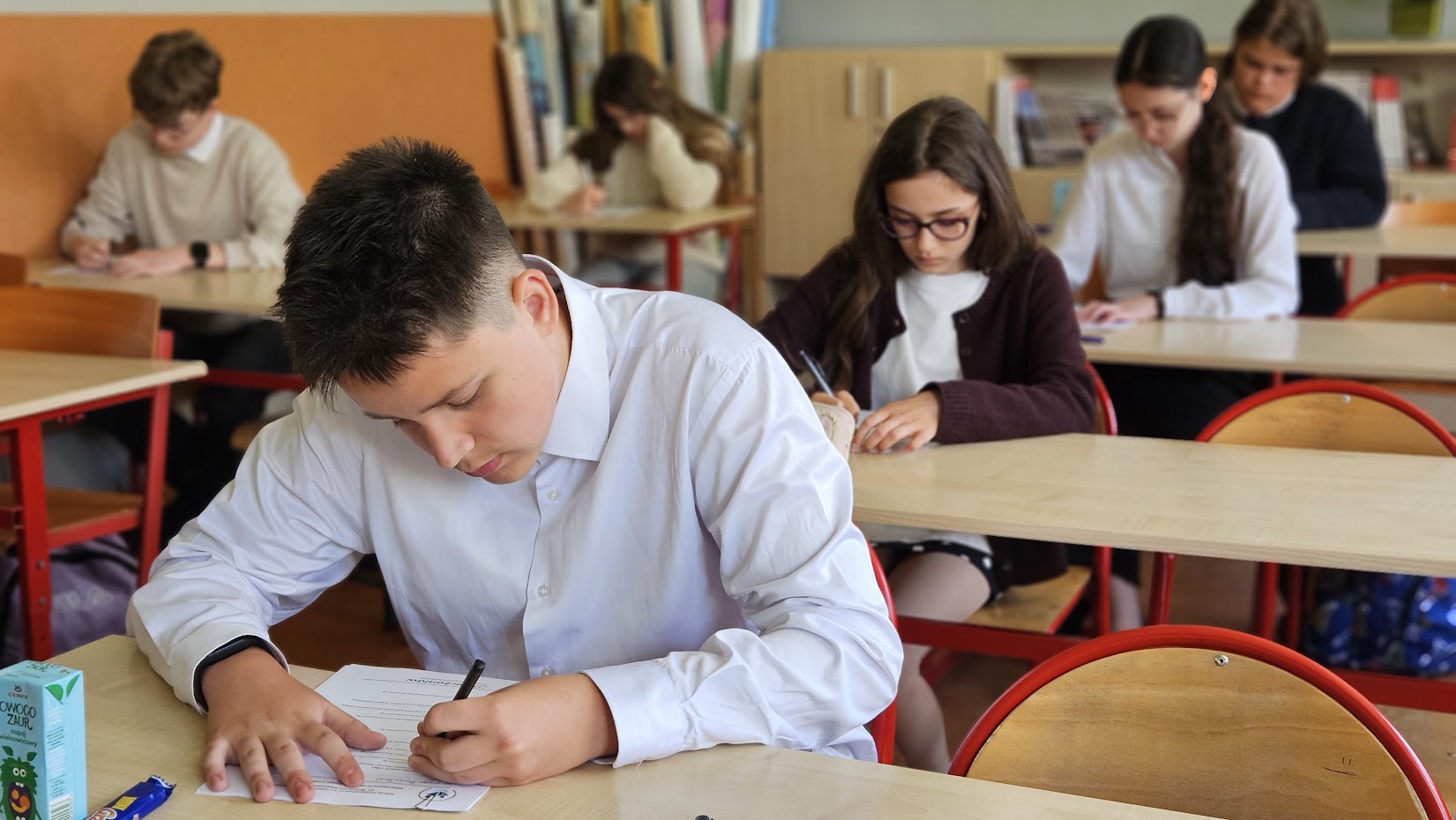 uczeń w klasie, w łąwce siedzi rozwiązuje test, za nim kolejni