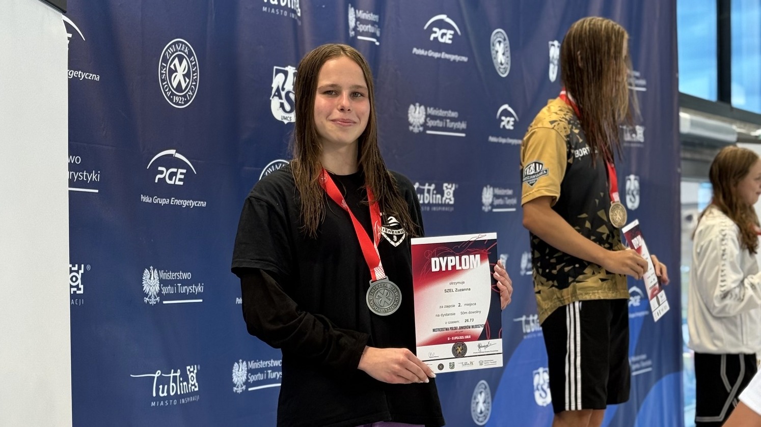 Zuzanna Szel na podium z dyplomem w ręce i z medalem na szyji
