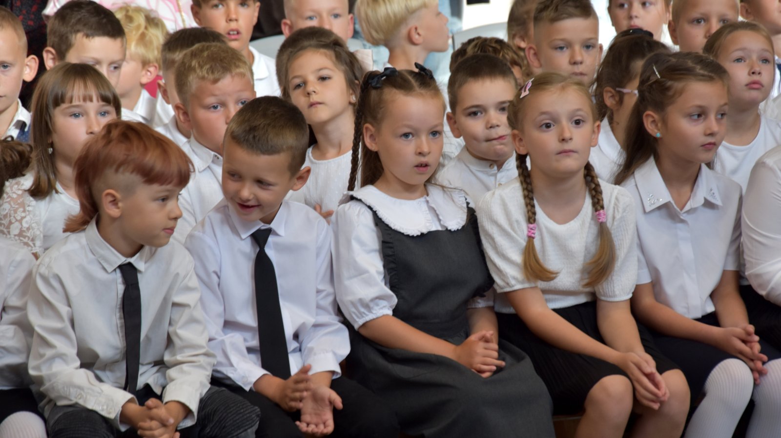Pierwszoklasiści w białych koszulokach siedzący na ławkach