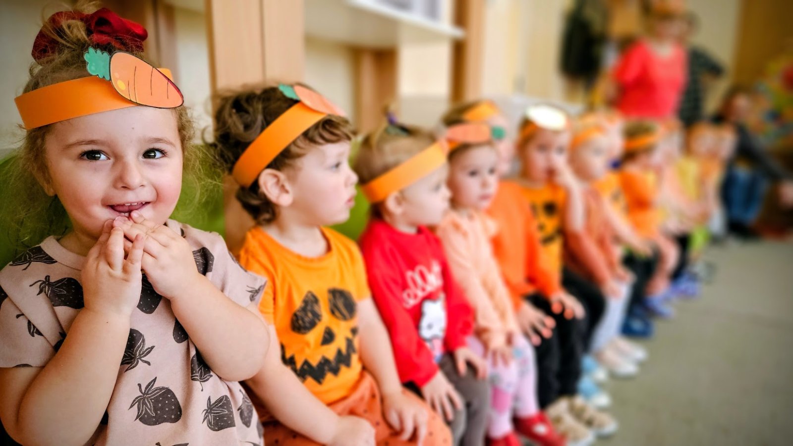 Małe dzieci siedzące na ławeczce, na pierwszym planie uśmiechnięta dziewczynka 