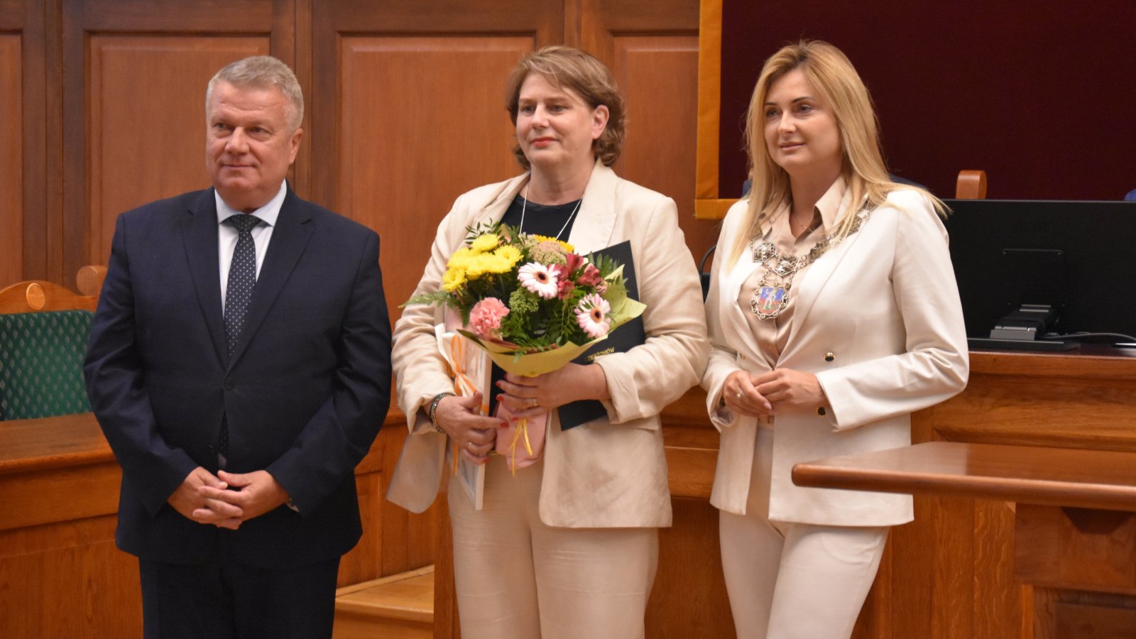 Odchodząca na emeryturę pani Iwona Cegiełka z bukietem kwiatów w dłoni z burmistrzem Dzierżoniowa Dariuszem Kucharskim i Przewodniczącą Rady Miejskiej Dzierżoniowa Agnieszką Denysiak.