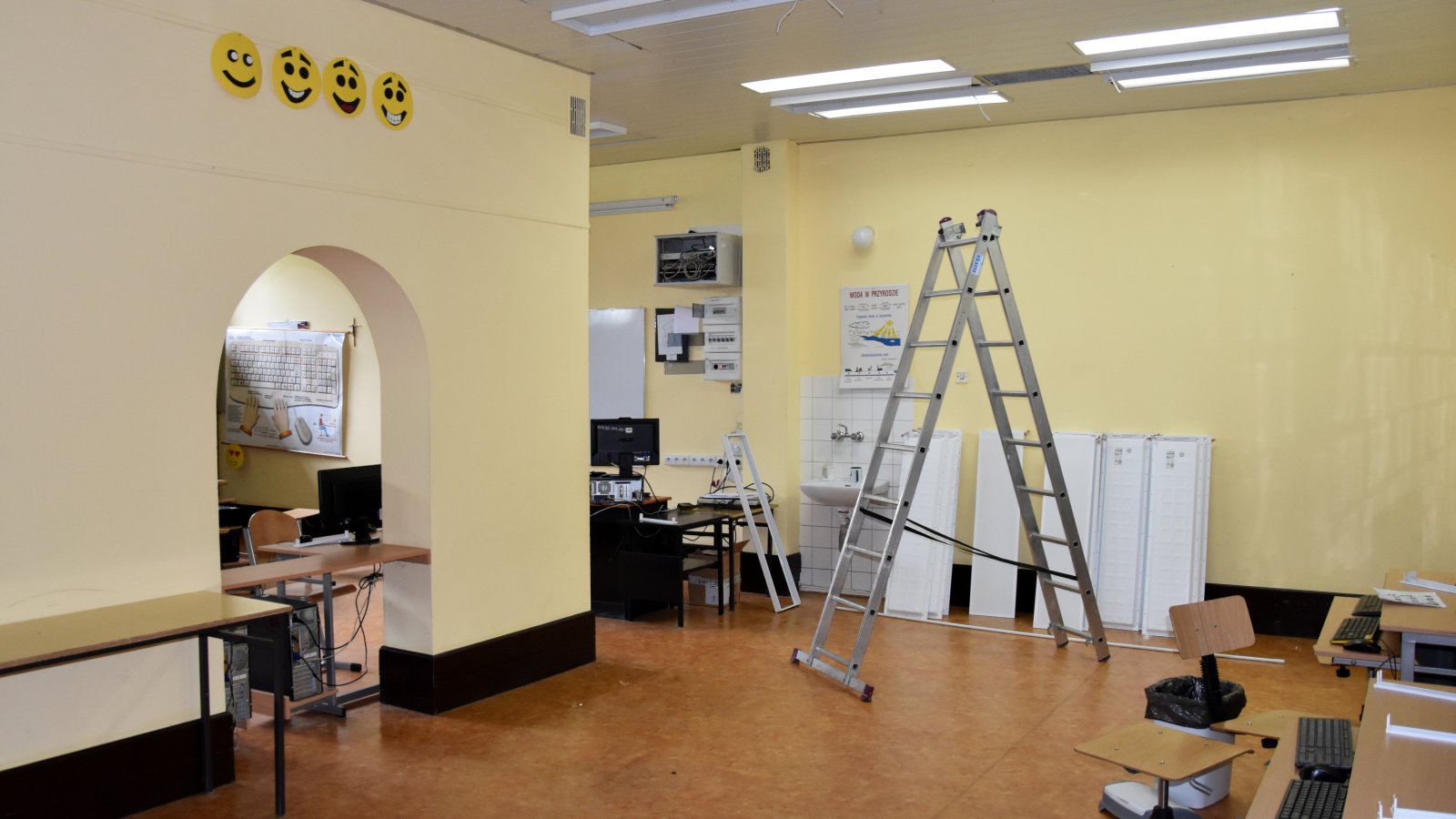 Klasa szkolna, przy ścianie ustawiona drabina, obok na ziemi stoją nowe lampy sufitowe