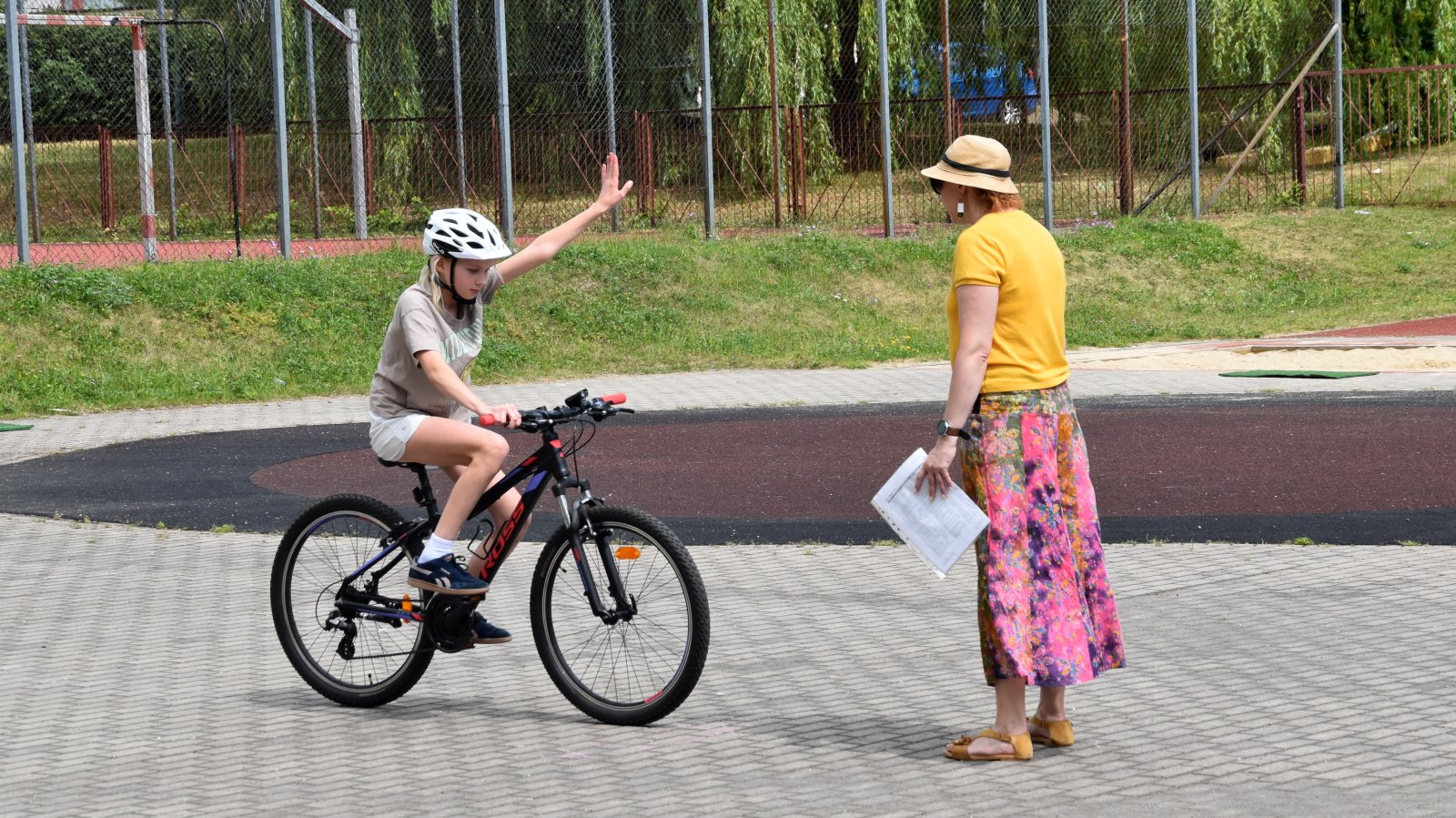 Dziewczyna na rowerze sygnalizująca ręką skręt w lewo, przy niej egzaminatorka