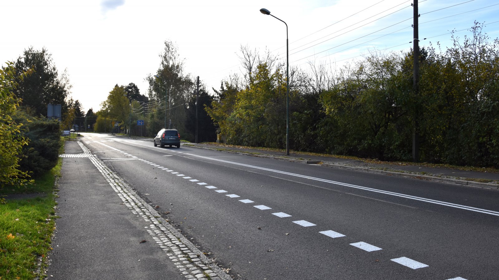 Droga i jeden jadący samochód, dookoła zieleń 