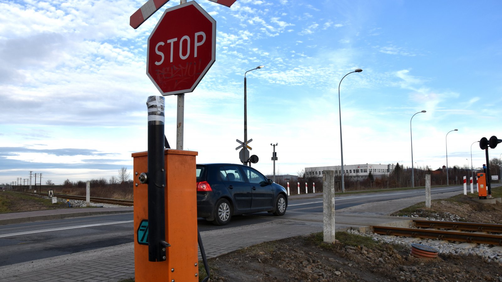 Auto na przejeździe kolejowym, obok znak Stop