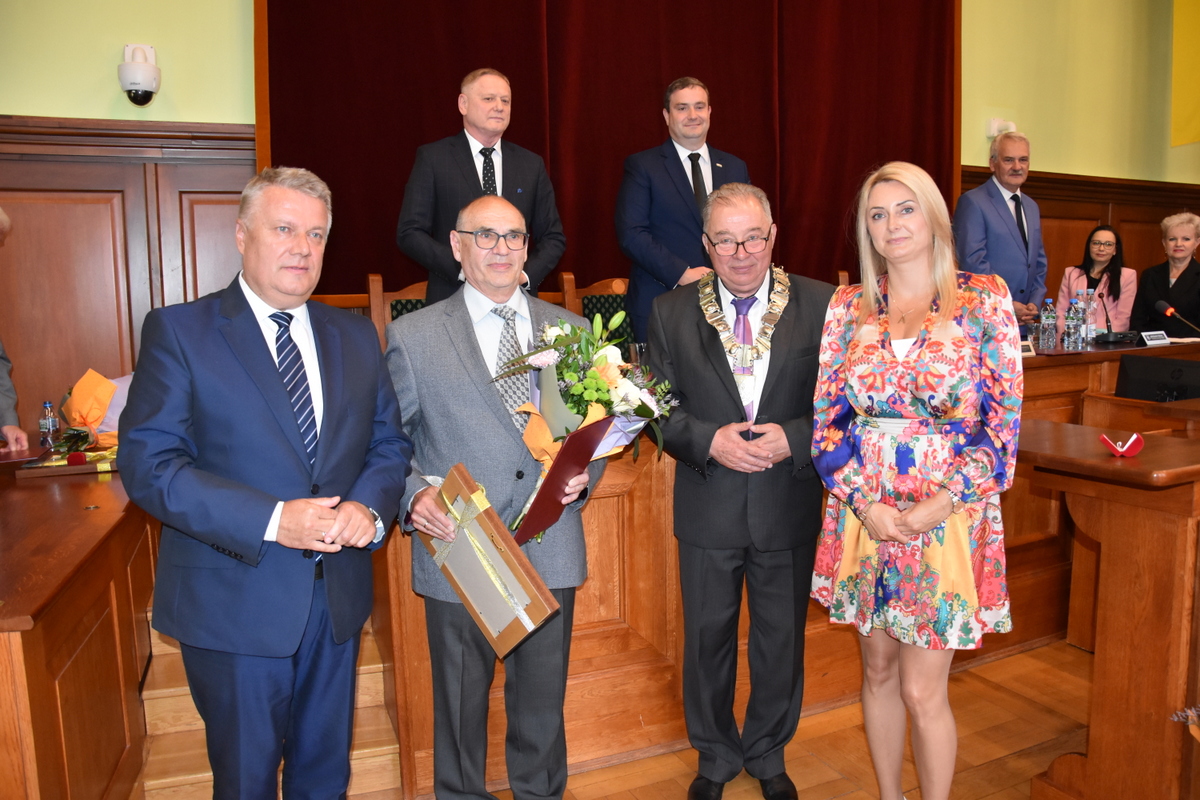 Siedem osób na wspólnym zdjęciu, jedna trzyma medal oprawiony w ramkę