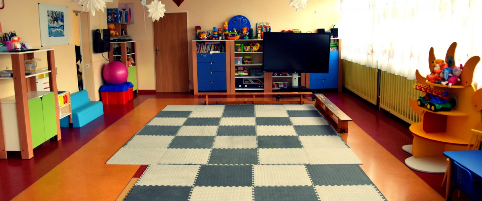 Sala zabaw dla małych dzieci, maty na podłodze, kolorowe zabawki, w tle duży telewizor