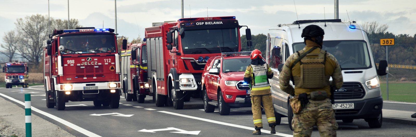 Wozy strażackie stojące na drodze, przed nimi strażak i żołnierz