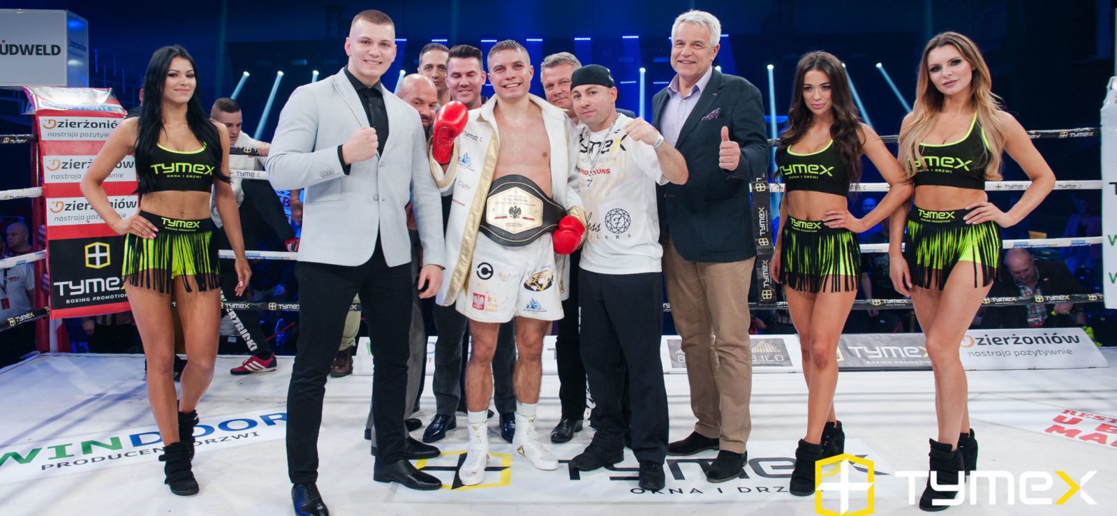 Grupa kobiet i mężczyzn na ringu bokserskim, pośrodku usmiechnięty zawodnik
