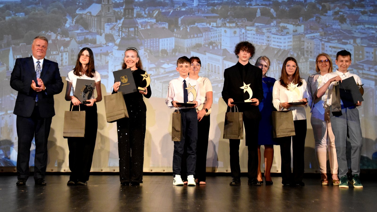 Uczniowie ze statuetkami, nauczyciele i burmistrz Dzierżoniowa, w tle zdjęcie miasta z góry