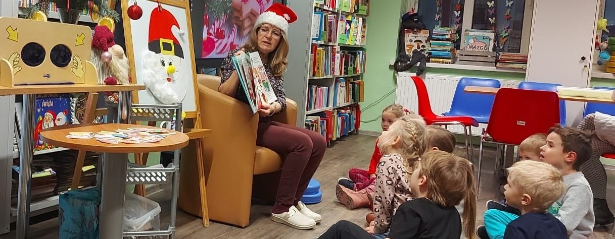 Grupa dzieci patrzy na bibliotekarkę z ksiązką w ręku