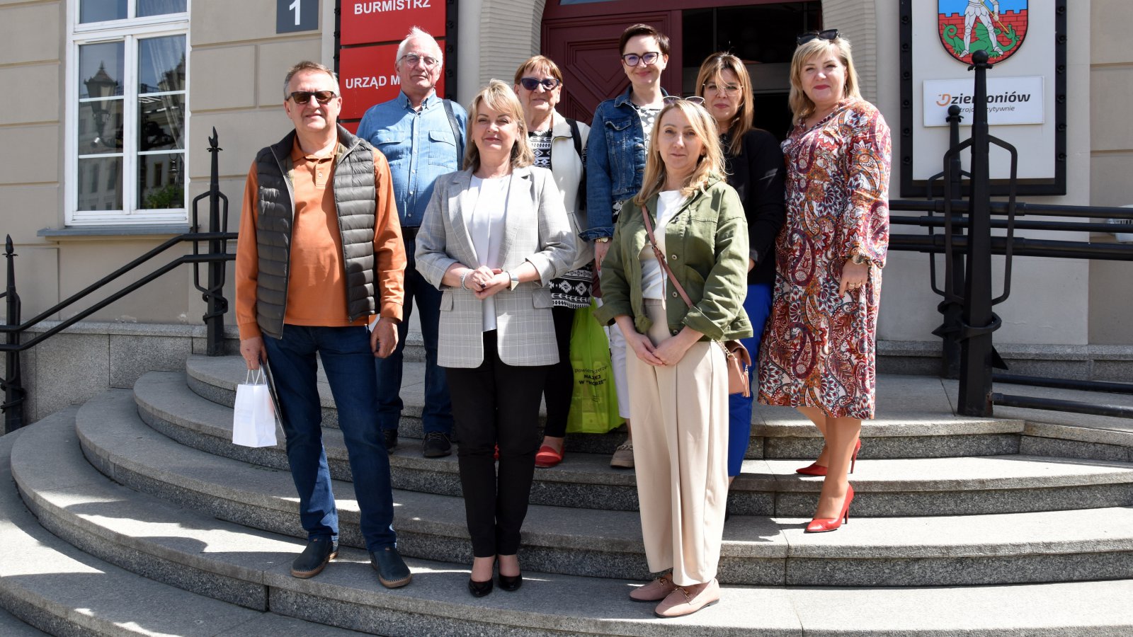 Grupa kobiet i mężczyzn stojąca na schodach prowadzących do budynku ratusza