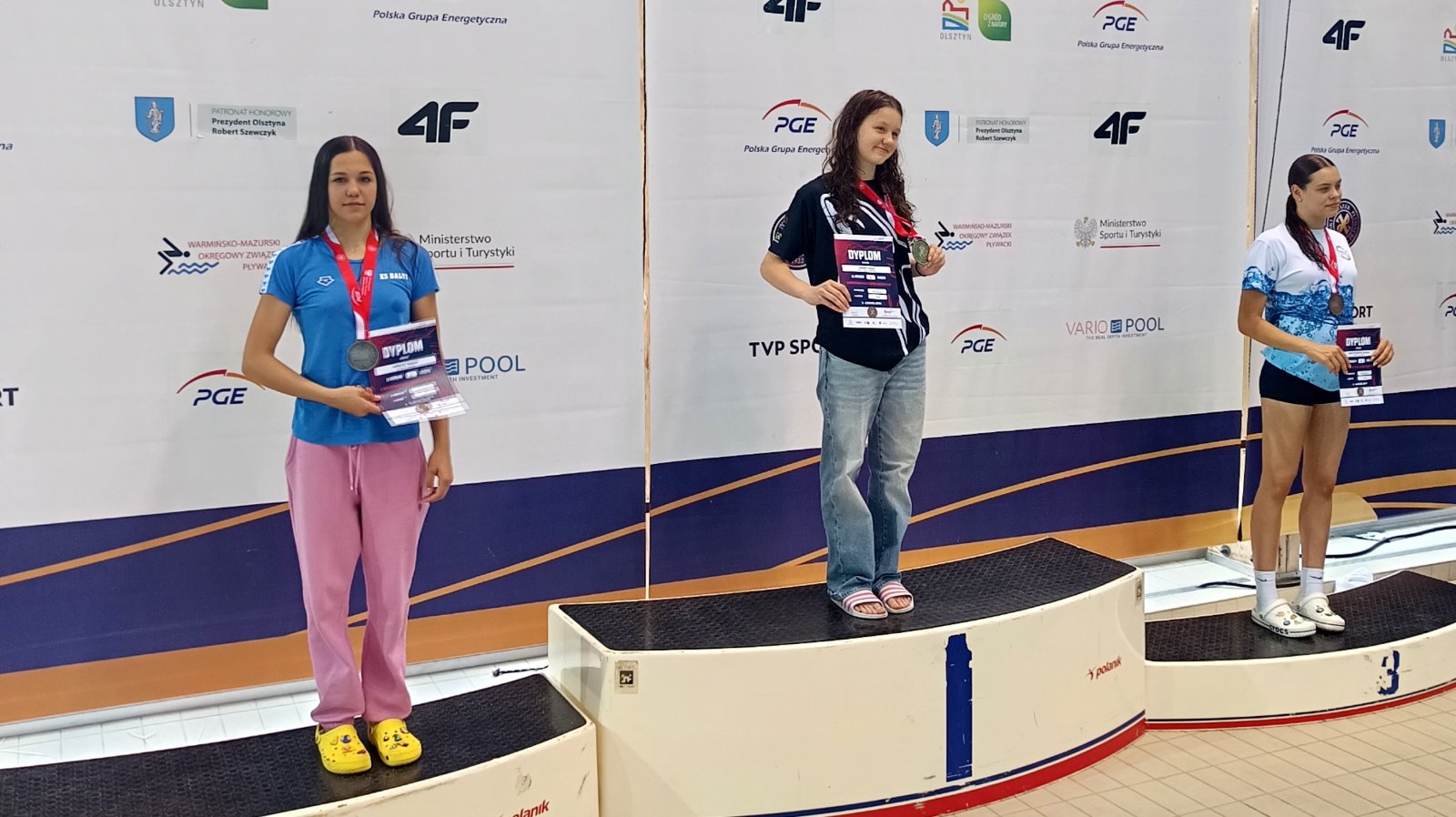 Natasza Paraciej (po lewej) stojąca na podium, obok dwie inne zawodniczki