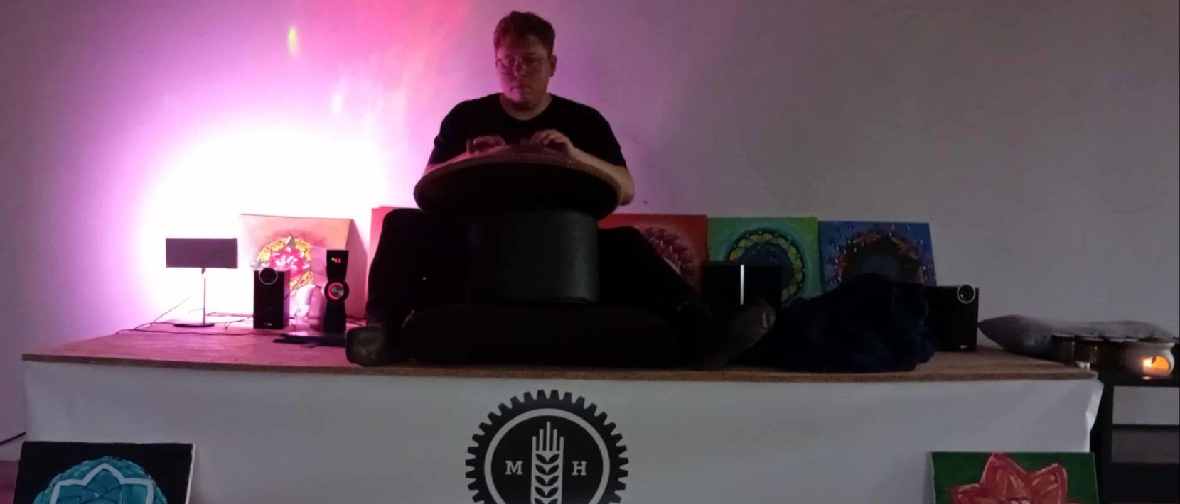 Artysta przy handpanie, różowe światło, na dole napis Młyn Hilberta