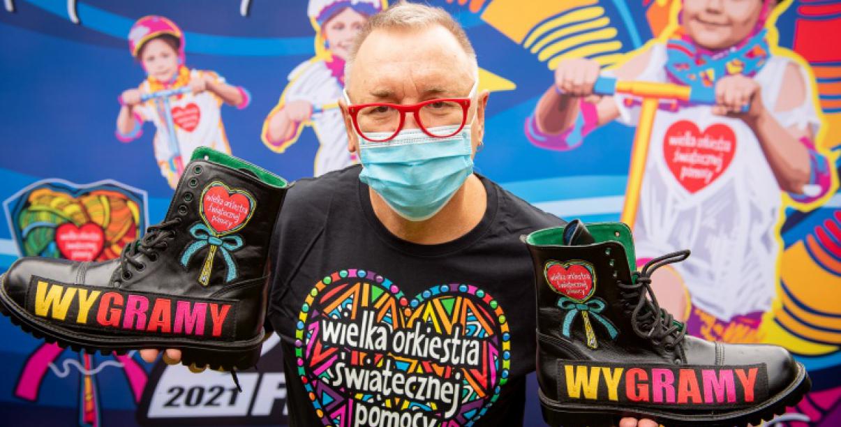 Jerzy Owsiak w maseczce, na tle plakatu WOSP.