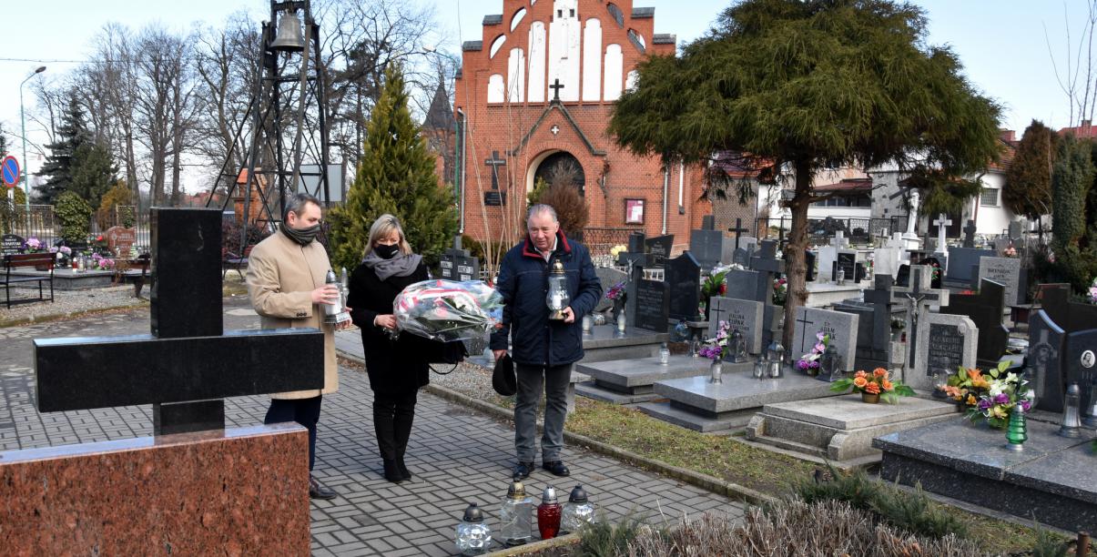 Trzy osoby składają wiążankę kwiatów przy pomniku na dzierżóniowskim cmentarzu 