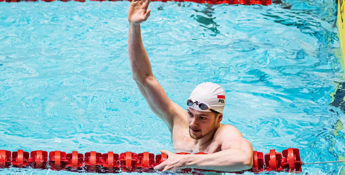 Paweł Juraszek w basenie z ręką podniesioną w geście zwycięstwa