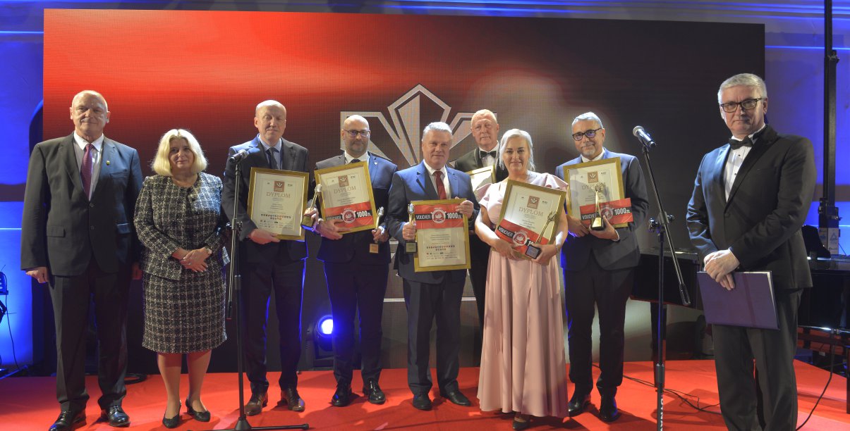 Grupa kobiet i mężczyn pozuje do wspólnego zdjęcia, czerwone tło