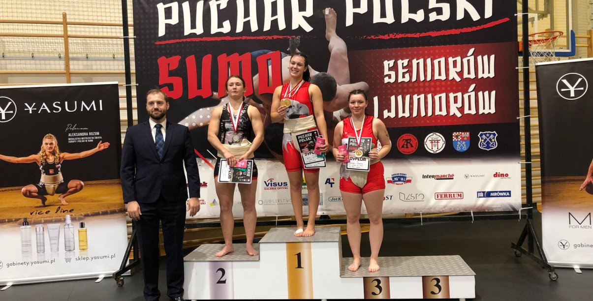 Trzy zawodniczki stojącfe na podium, obok mężczyzna w garniturze