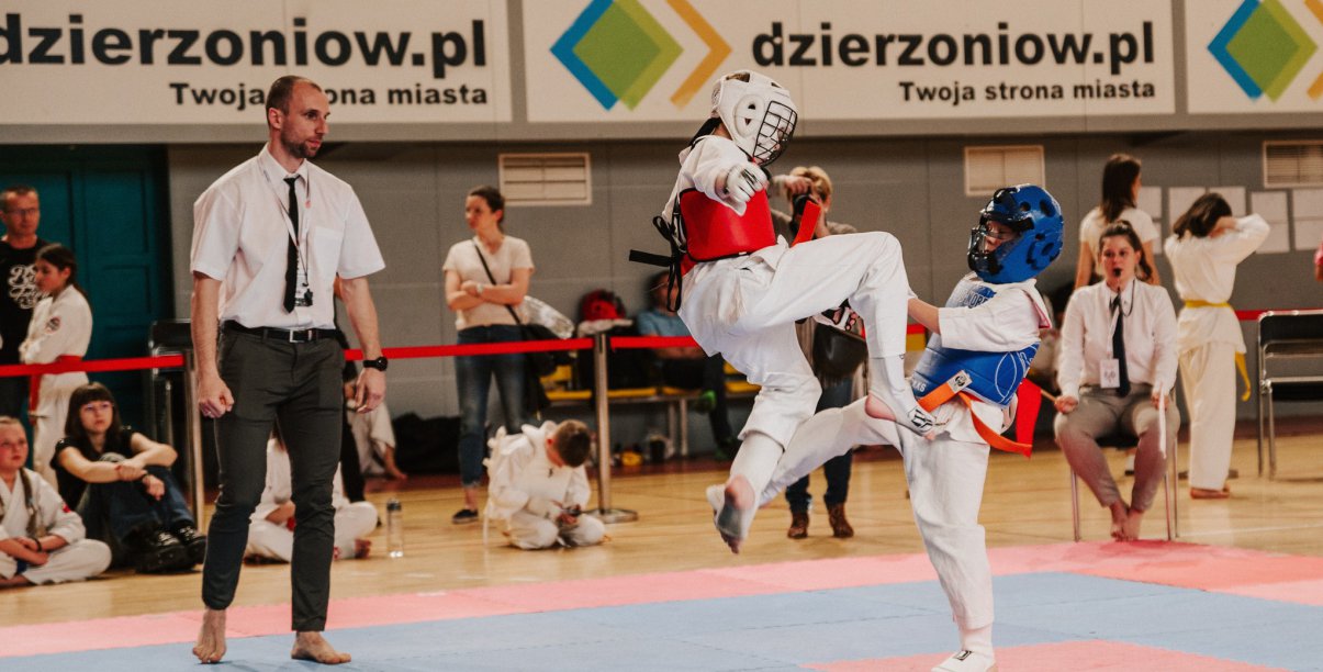 Karateka z wyskoku atakuje przeciwnika, obok sędzia
