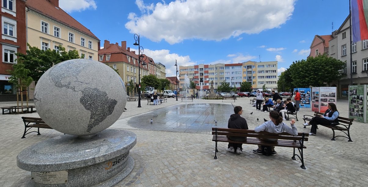 Rynek, ludzie siedzący na ławkach, po lewej ogromny kamienny globus