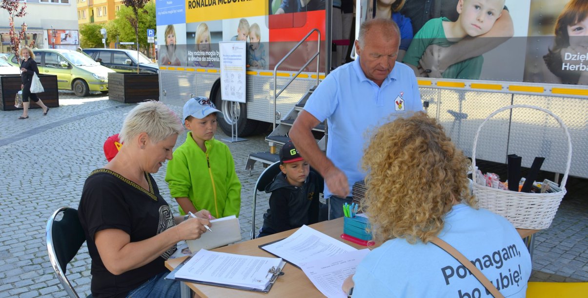 Rejestracja przed ambulansem fundacji Ronalda McDonalda w dzierżoniowskim Rynku, Kobieta i mężczyzna z dziećmi są przyjmowani w rejestracji