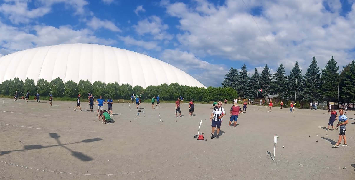 Duży plac, ludzie grający grupkami w petanque