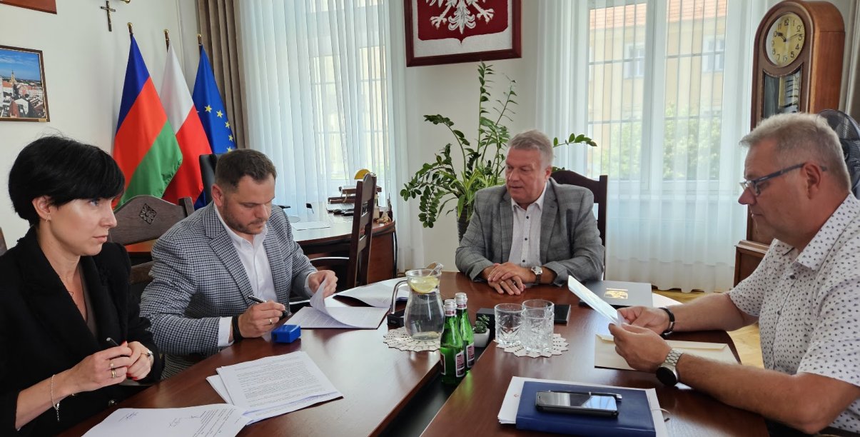Cztery osoby, w tym burmistrz miasta Dariusz Kucharski (w środku), podpisują dokumenty przy stole w gabinecie burmistrza Dzierżoniowa