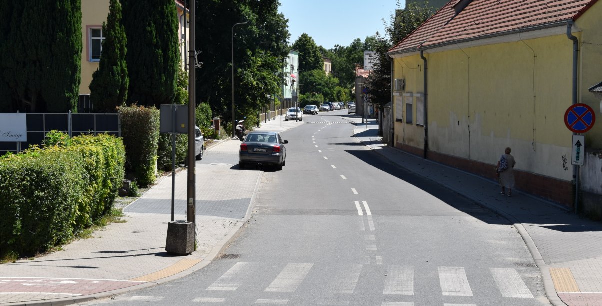 Ulica Słowiańska, na pierwszym planie przejście dla pieszych, na chodniku po lewej zaparkowane auta, obok zieleń