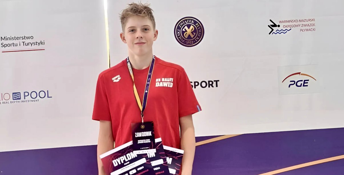 Dawid Opaliński w czerwonej koszulce z medalem na szyi i z dyplomami w rękach
