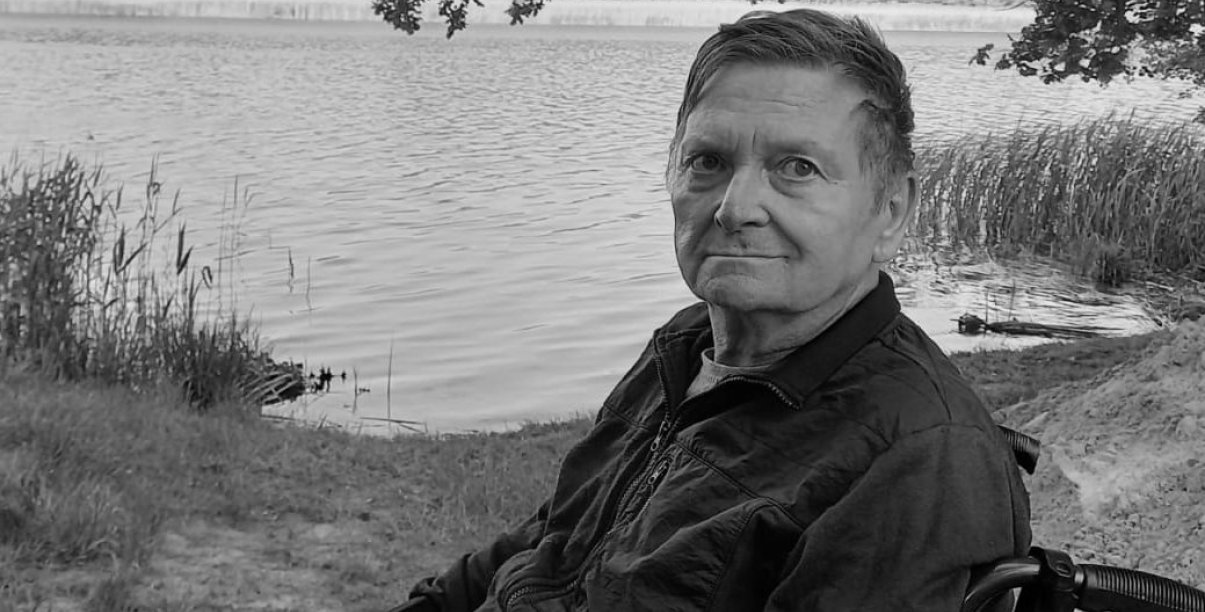 Czarno-białe zdjęcie mężczyzny na wózku inwalidzkim, w tle zbiornik wodny