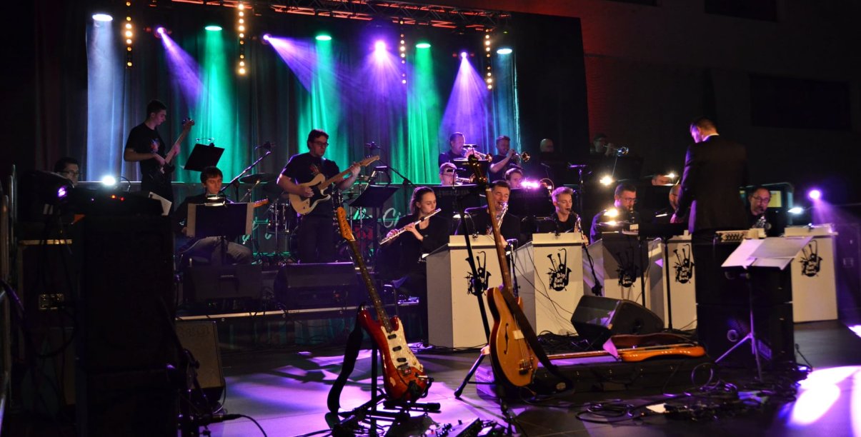 Muzycy Big Roll Band na oświetlonej scenie, pzred nimi dyrygent i instrumenty