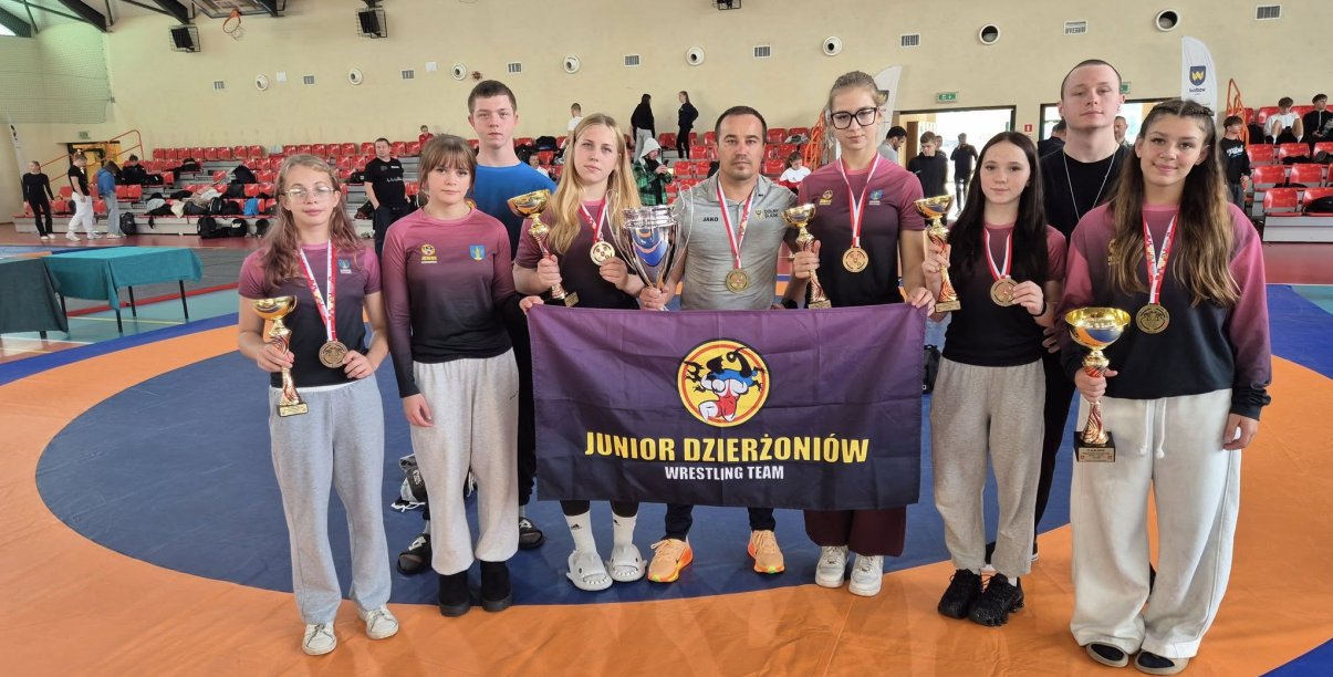 grupa 5 zapaśniczek z medalami i pucharami z trenerami i flagą klubu sportowego Junior Dzierżoniów