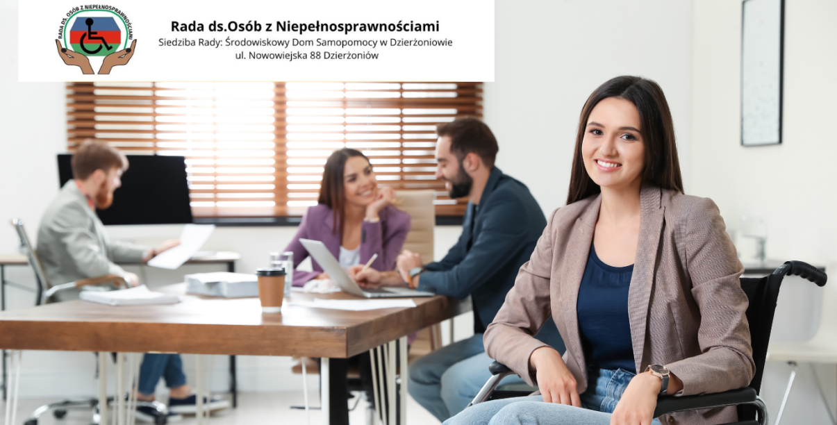 Biuro, osoby rozmawiające przy stole, na pierwszym planie uśmiechnięta, siedząca na wózku niepełnosprawna kobieta