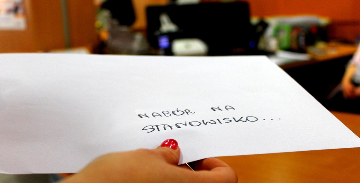 Ręka z kopertą z napisem "Nabór na stanowisko" na tle Biura Obsługi Klienta