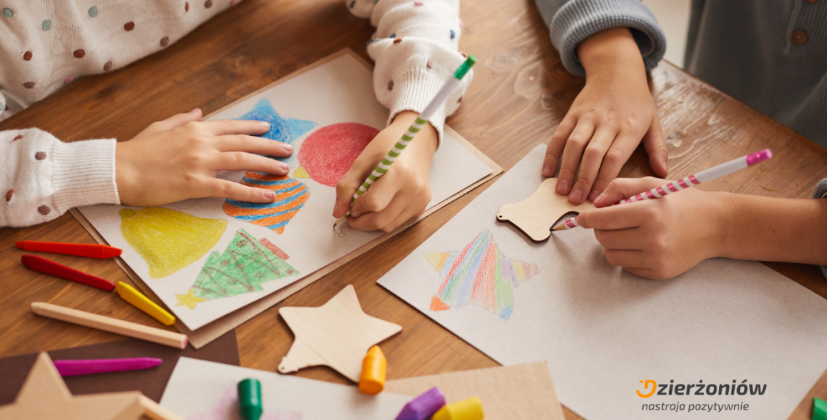 Ręce siedzących przy stole dzieci rysujących świąteczne elementy na kartkach papieru