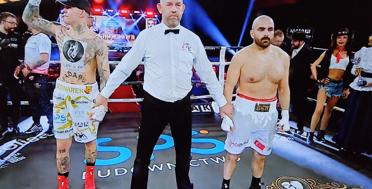 Ring bokserski, po wygranej walce dwaj bokserzy z sędzią, Kamil Bednarek unosi zaciśniętą rękę do góry w geście zwycięstwa