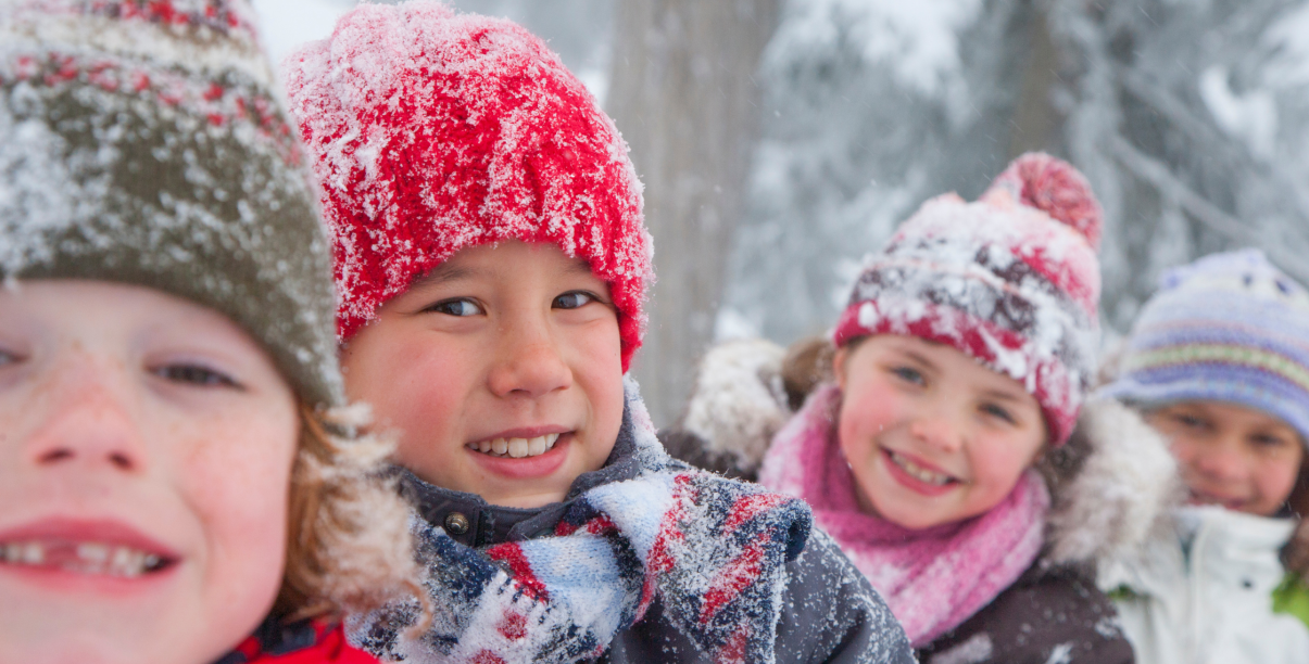Czworo uśmiechniętych dzieci w zimowej scenerii, w ośnieżonych czapkach