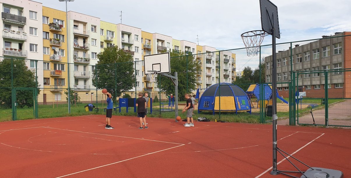 Czwórka chłopców na boisku do kosza, za nimi długi blok