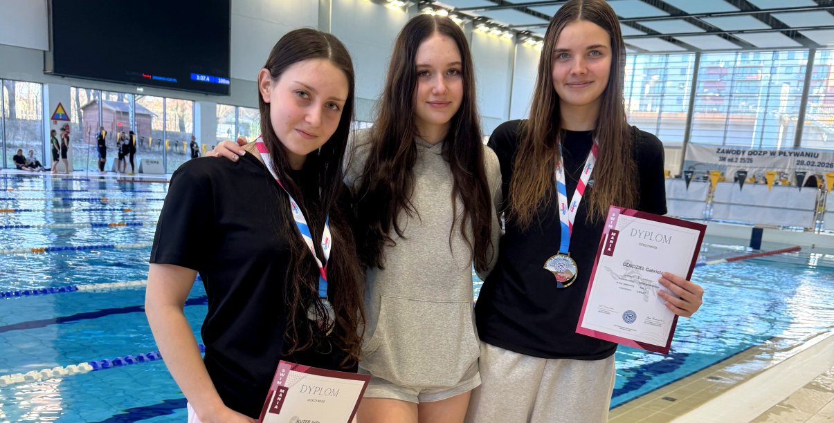 Trzy pływaczki, w tym dwie z dyplomami, na tle basenu