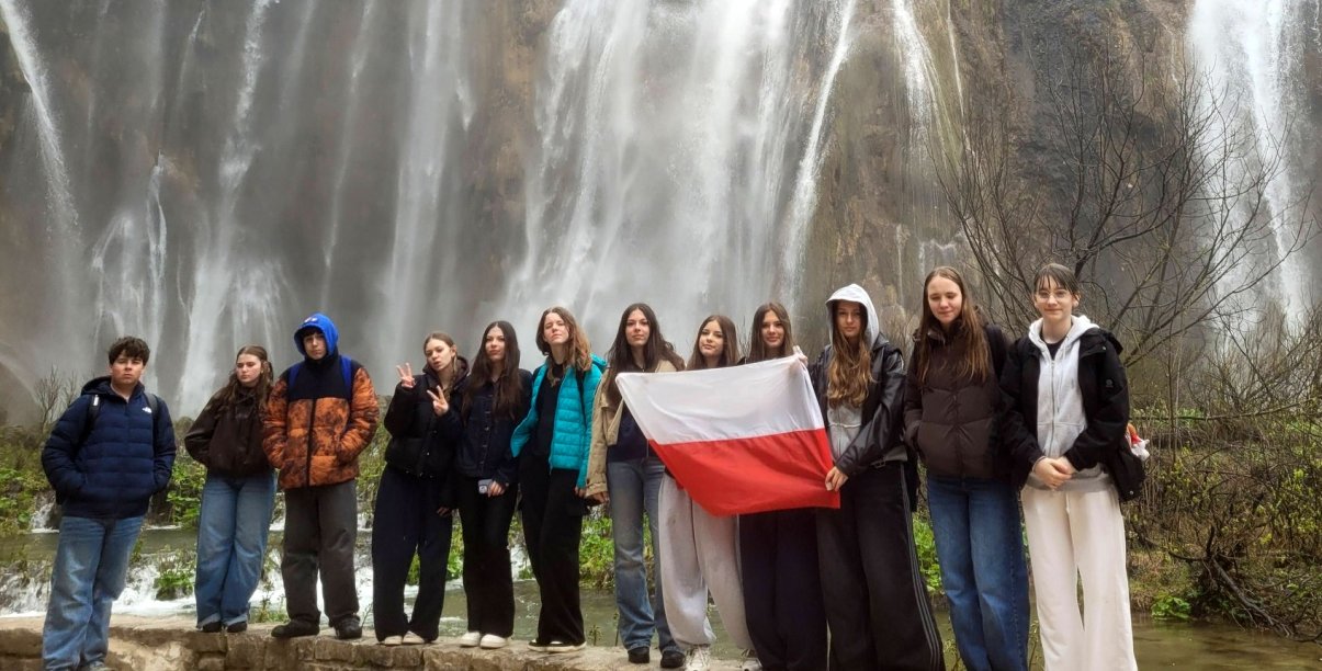 Uczniowie na wspólnym zdjęciu z flagą Polski, na drugim planie wodospad