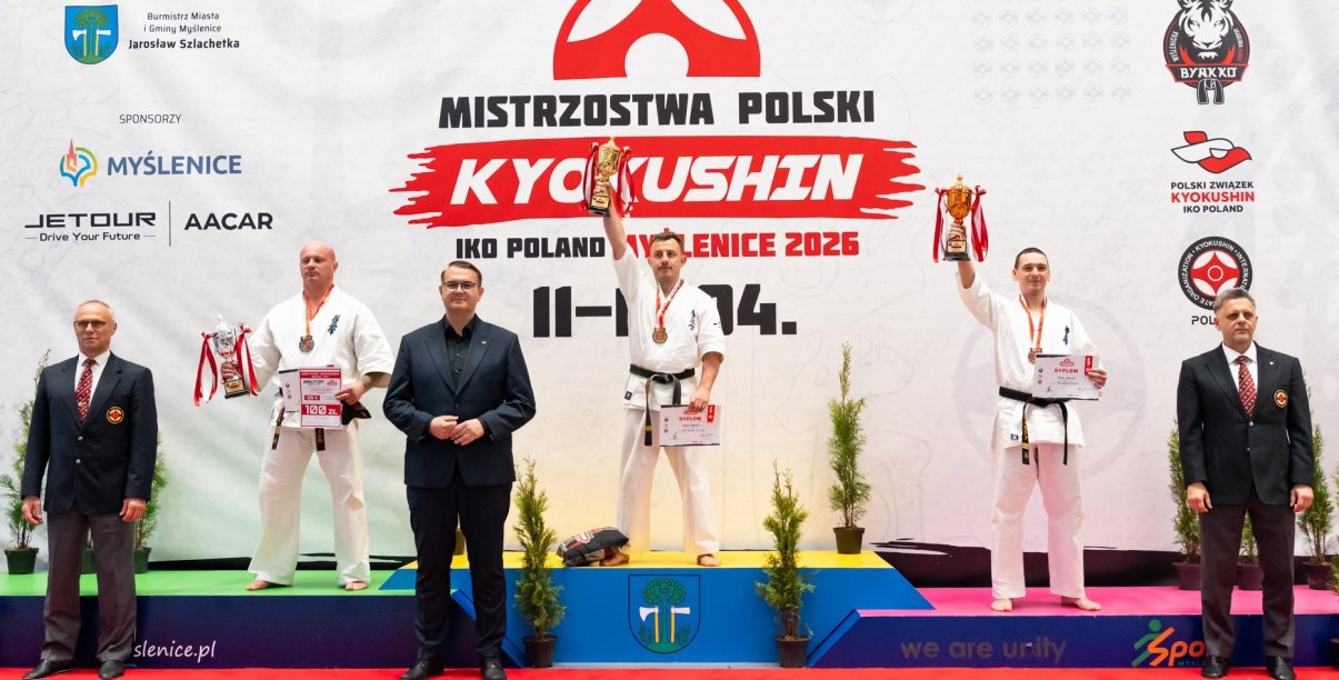 Trzech karateków na podium, Tomasz Staściuk na pierwszym miejscu z uniesionym w górę pucharem 