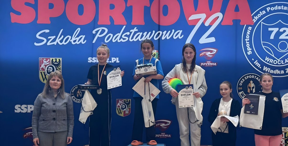 Pięć zawodniczek, trzy stoją na podium, dwie obok, niebieskie tło