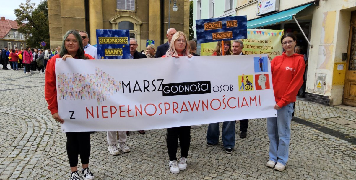 Trzy dziewczyny trzymające baner z napisem "Marsz osób z niepełnosprawnościami"