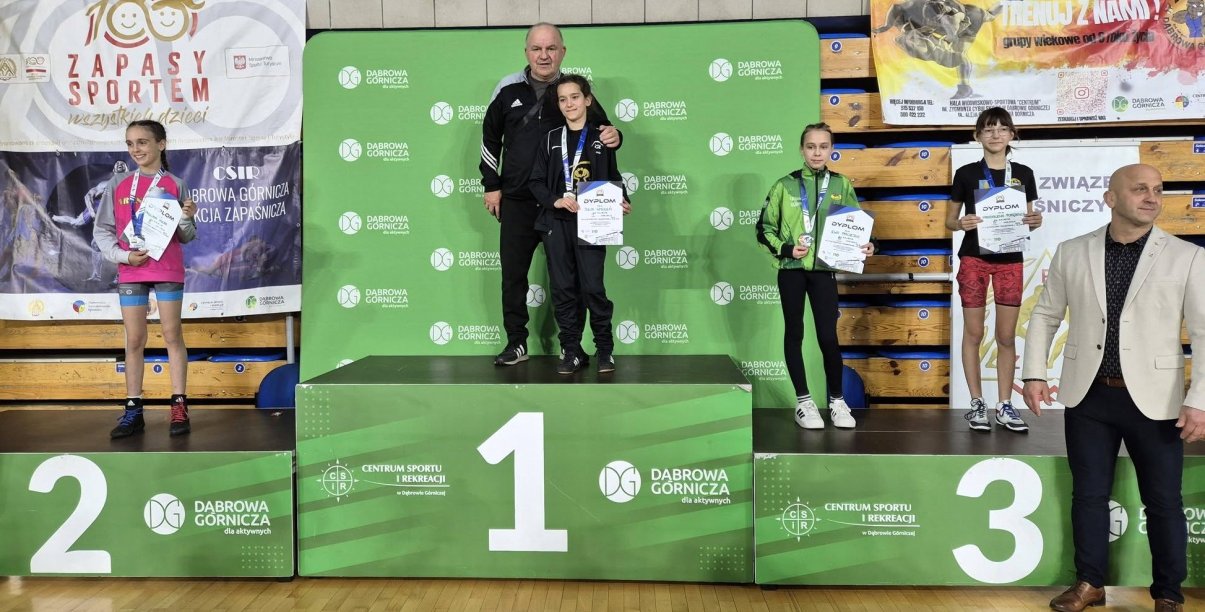 Zawodniczki stojące na zielonym podium z medalami i dyplomami