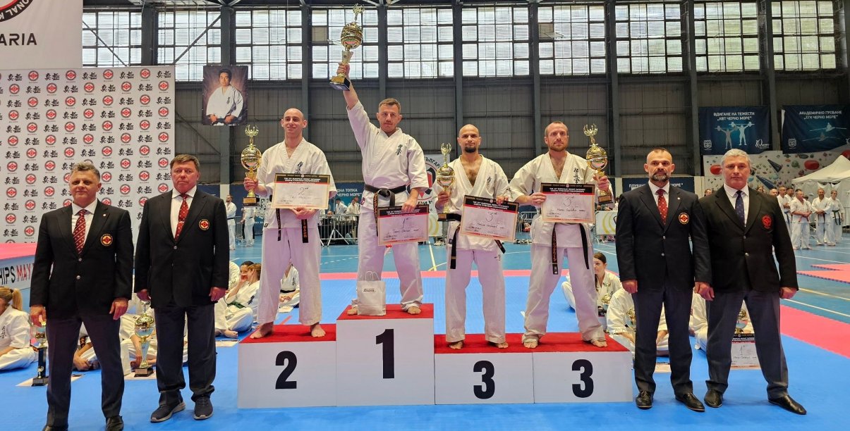 Czwórka zawodników w strojach do karate stoi na podium. Na najwyższym stopniu Tomasz Staściuk z uniesionym do góry pucharem