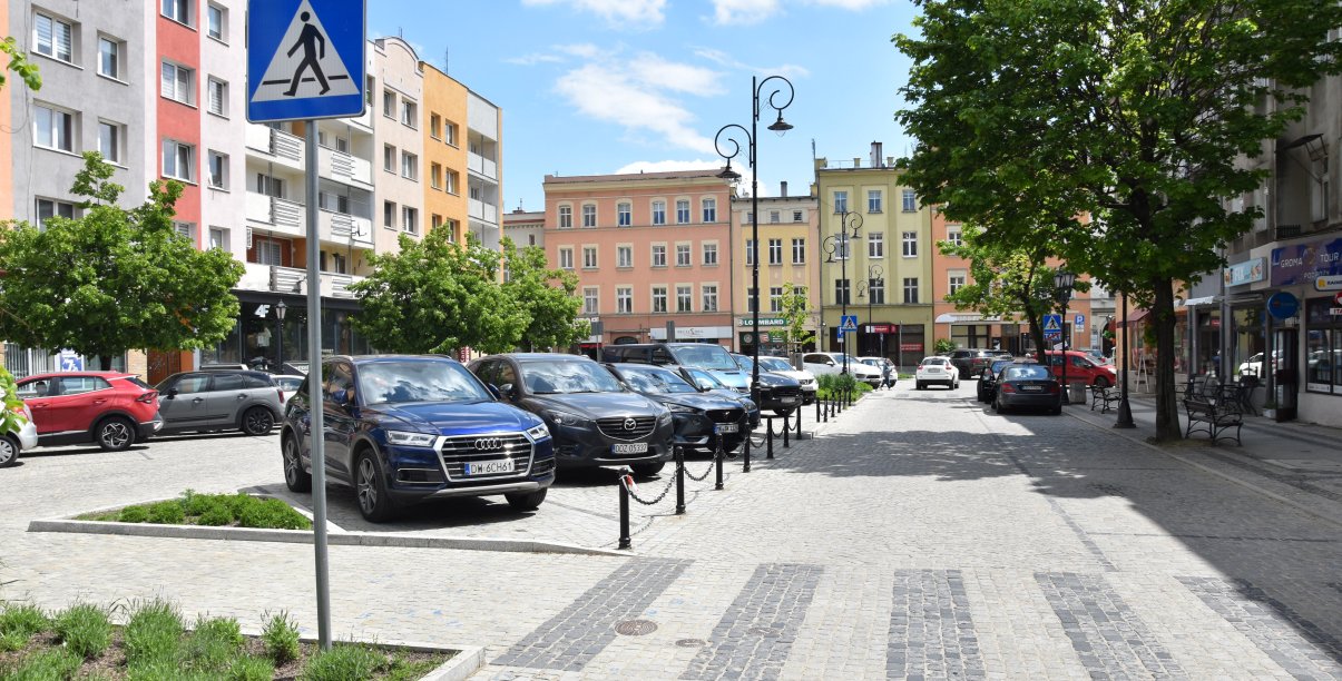 Rynek, zaparkowane samochody, w tle budynki, na pierwszym planie przejście dla pieszych